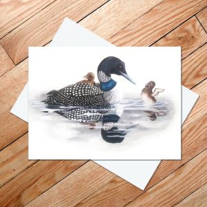 Greeting card of a mama loon eyeing her independent chick, while the other rides on her back