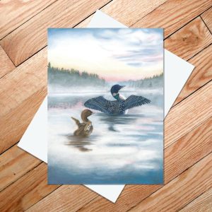 Greeting card of baby and adult loon raising their wings in the morning mist