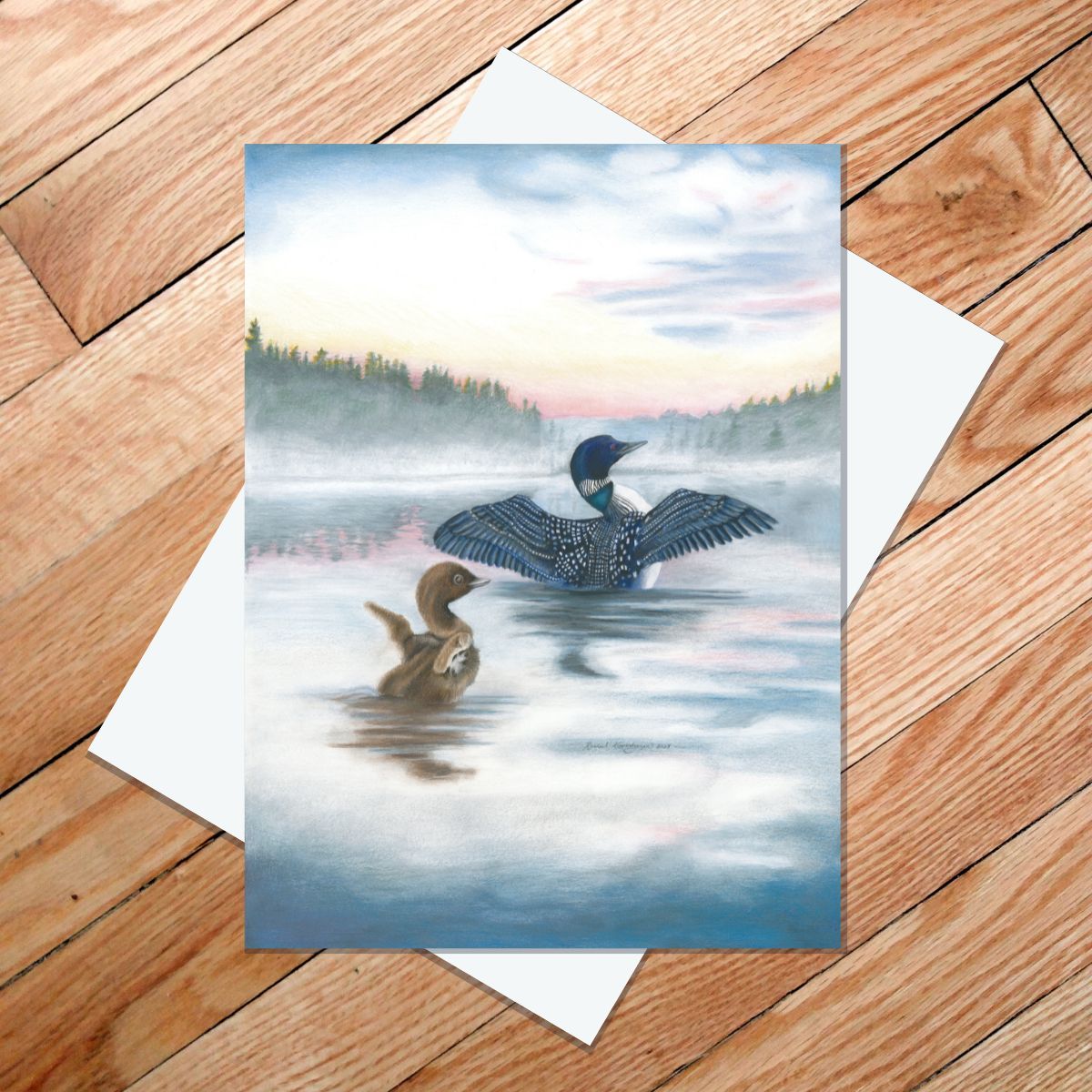 Greeting card of baby and adult loon raising their wings in the morning mist