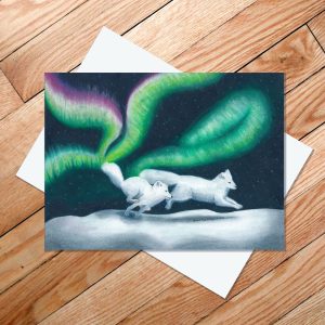 Greetiing card of two arctic foxes racing across the snow as their tails spark the northern lights